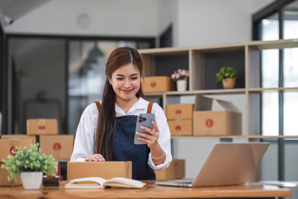 Mujer emprendedora preparando paquetes y utilizando el celular