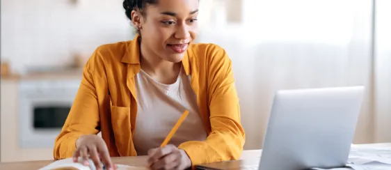 Mujer joven viendo una laptop y tomando anotaciones en una libreta