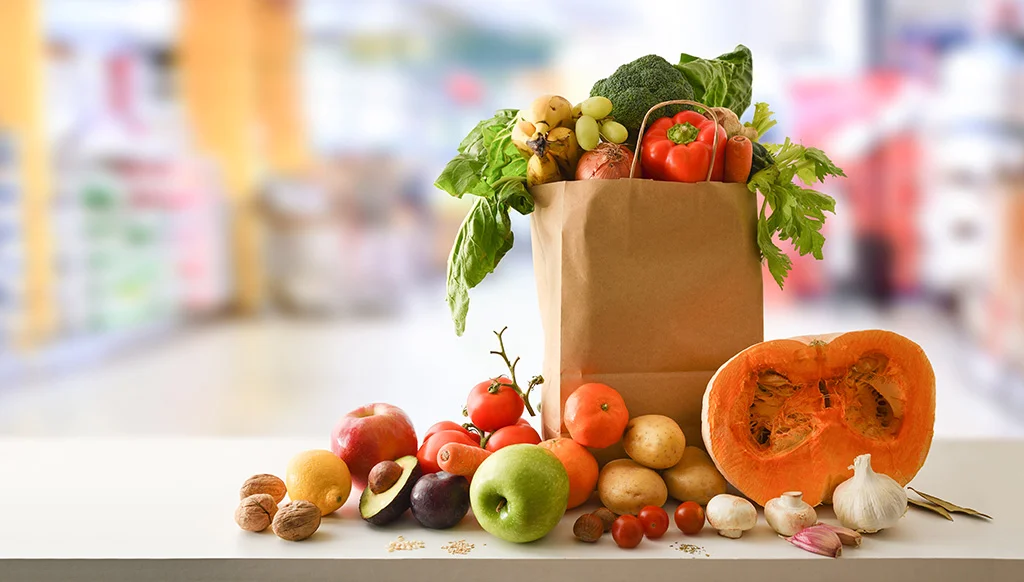 Bolsa de papel sobre una mesa llena con frutas y verduras