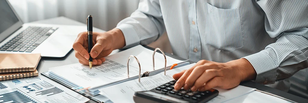 Persona escribiendo sobre un papel y en la misma mesa una calculadora